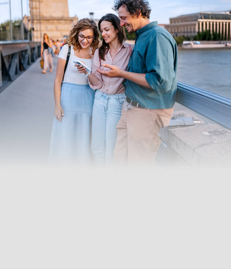 Zwei Frauen und ein Mann stehen lächelnd nebeneinander und schauen auf ihr Handy