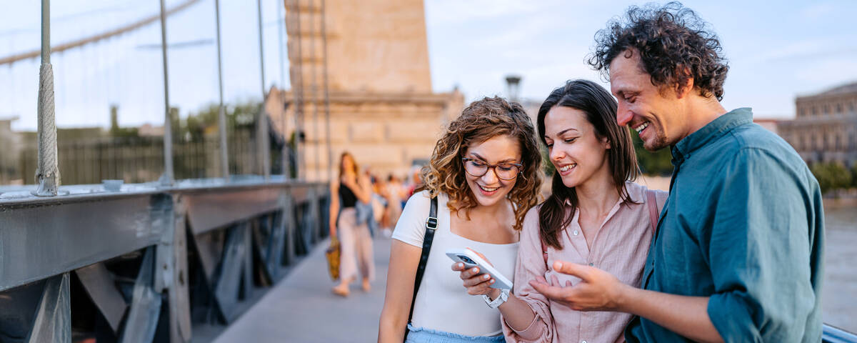 Zwei Frauen und ein Mann stehen lächelnd nebeneinander und schauen auf ihr Handy