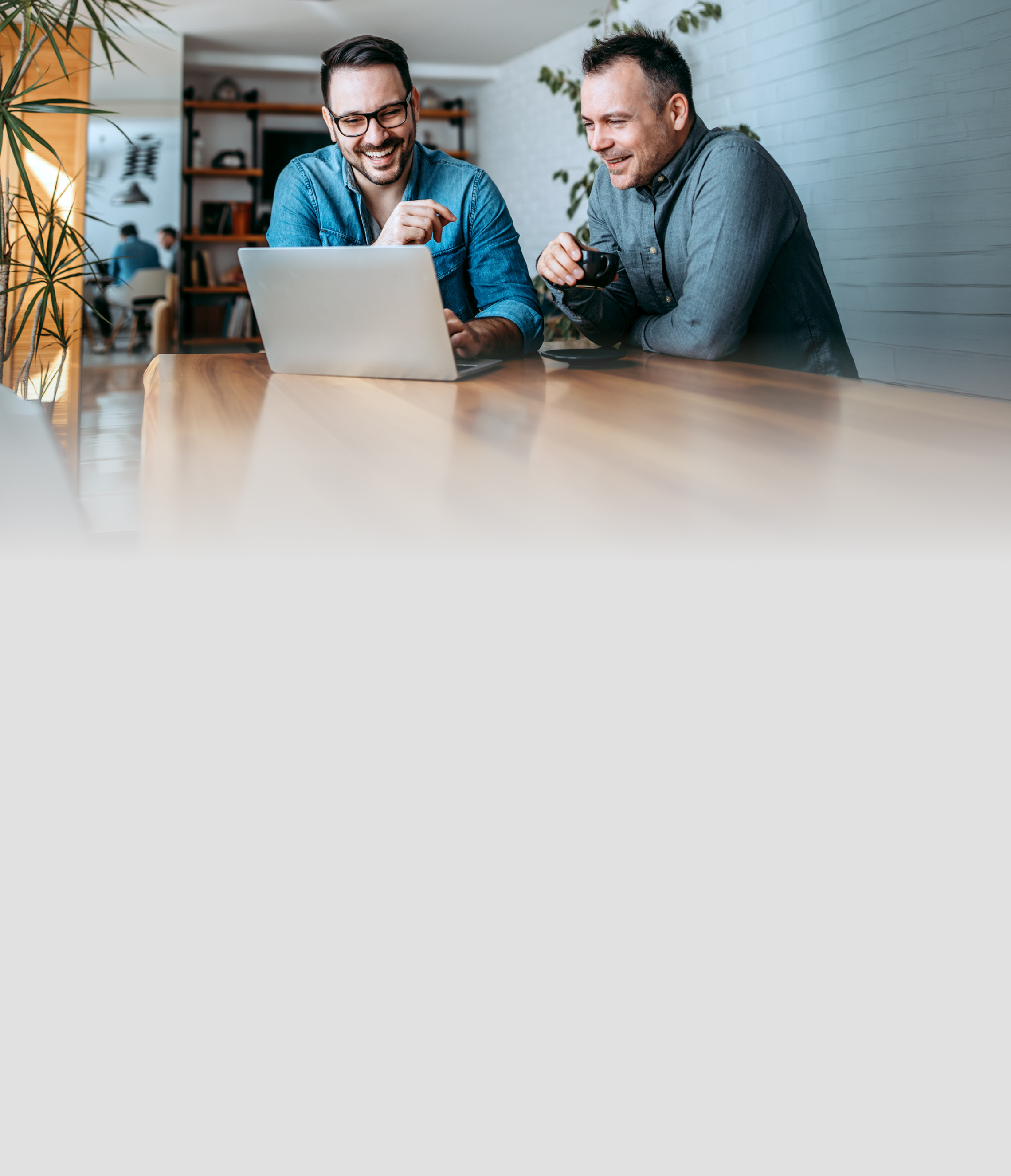 Zwei Männer lächeln während sie auf den Laptop schauen.