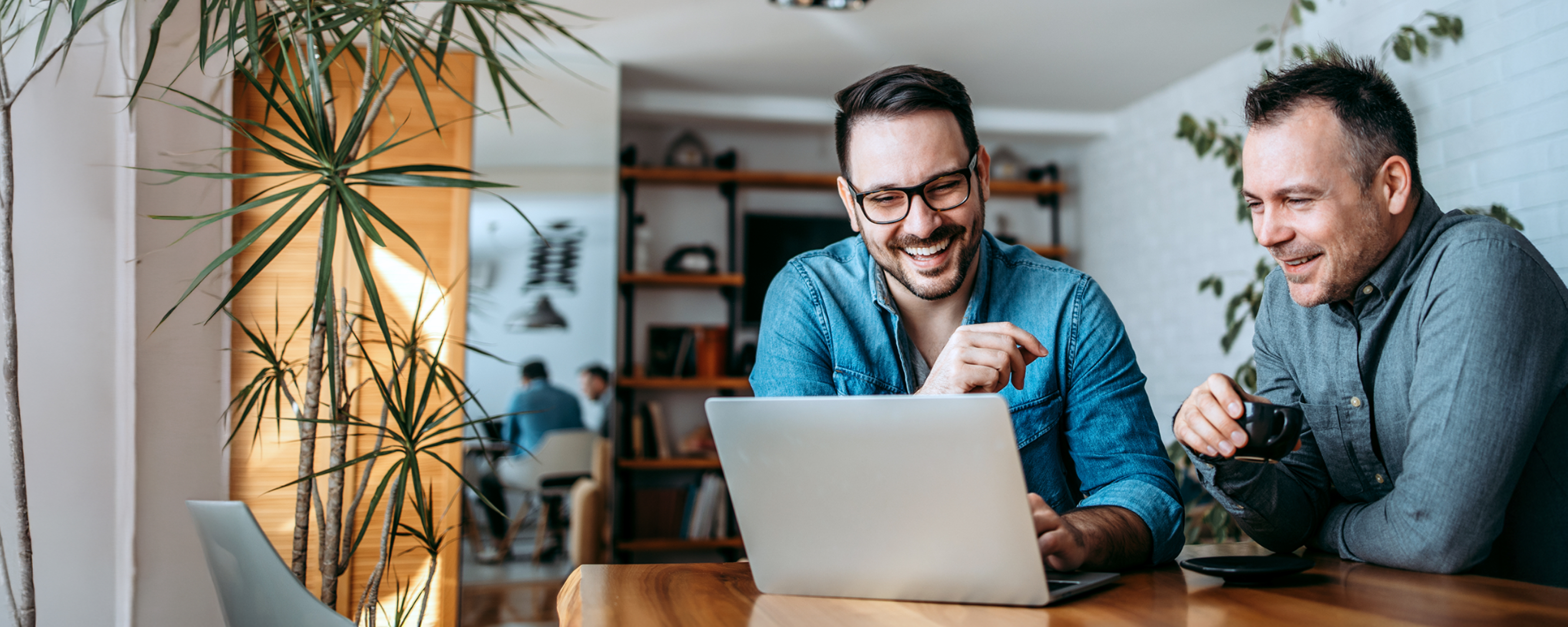 Zwei Männer lächeln während sie auf den Laptop schauen.